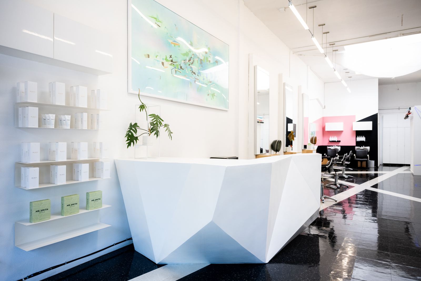 The faceted white reception desk with product shelves and a large abstract painting
